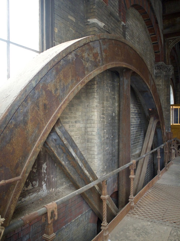 A rusted wheel with three large spokes visible, with the remainder of the wheel below the floor.